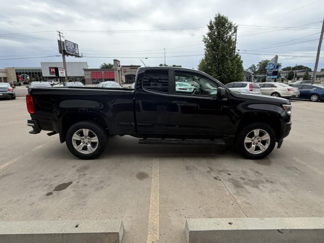 Black four-door pickup truck parked in a dealership lot, seen from the side with chrome wheels and running boards.