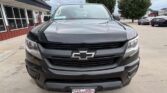 Front view of a black Chevrolet pickup truck parked outside a dealership, showing the Chevy emblem on the grille.