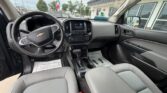 Interior view of a Chevrolet SUV dashboard, steering wheel with bowtie emblem, center touchscreen, and gear shifter visible between gray cloth seats.