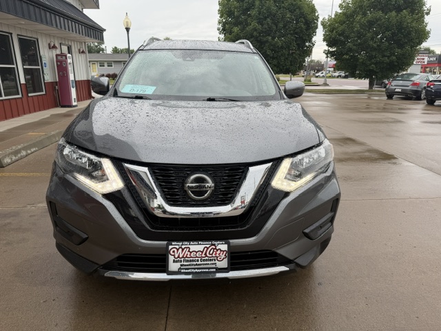 Front view of a gray Nissan SUV on a wet dealership lot, showing the V‑motion grille and headlights, with a Wheel City Auto Finance Centers license plate frame.