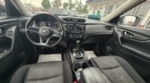Interior of a Nissan sedan: black driver and passenger seats, steering wheel, gear shifter, and dashboard with touch screen, seen from the front passenger seat in rainy conditions.