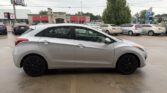 Side view of a silver compact car parked in a dealership lot with other vehicles in the background.