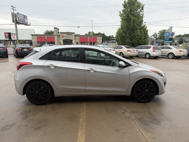 Side view of a silver compact car parked in a dealership lot with other vehicles in the background.