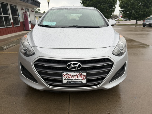 Front view of a silver Hyundai at a dealership, with a Wheel City Auto license plate, on wet pavement with storefronts and trees in the background.