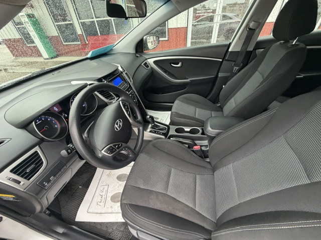 Inside a gray Hyundai sedan: front seats with black fabric, steering wheel with Hyundai logo, and center console with gear shifter visible