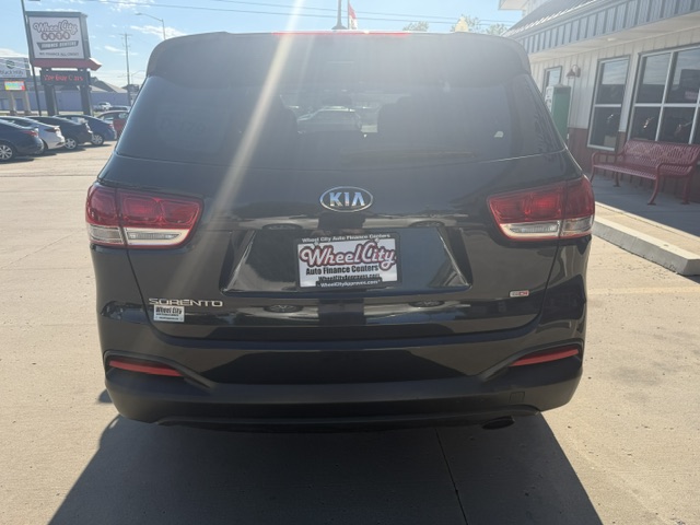 Rear view of a black Kia Sorento SUV in a dealership lot, with a Wheel City Auto Finance Centers license plate frame and showroom building in the background.