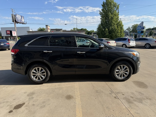 Side view of a black mid-size SUV parked in an outdoor lot, with yellow parking lines and other cars and trees in the background.