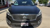 Front view of a black Kia SUV parked outside a dealership on a sunny day, displaying the distinctive grille and a Wheel City license plate frame.