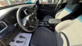 Interior of a modern SUV: steering wheel, dashboard, center console, and gray cloth front seats visible from the driver’s side window. A floor mat with footprints is on the driver's side. Outside scenery seen through the windshield.
