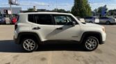 Side profile of a white Jeep Renegade SUV parked in a sunny parking lot, with other cars and a few buildings in the background.