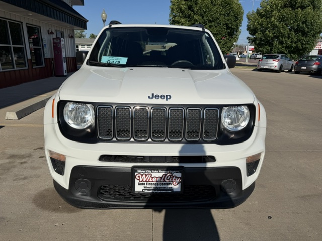 Front view of a white Jeep SUV with seven-slot grille parked in a dealership lot; price tag visible on the windshield.