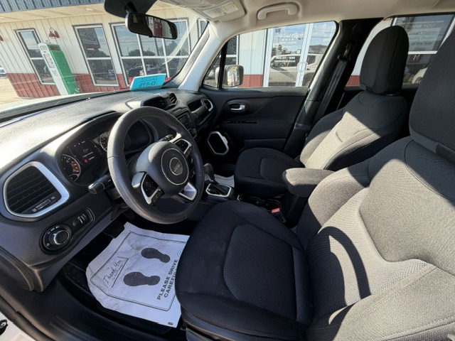 Front cabin view of a black SUV with steering wheel (Jeep logo), dashboard, gear shifter, and fabric driver/passenger seats in a dealership setting.