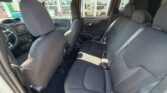 View of a car’s interior from open rear door: dark fabric seats, front driver seat, and a rear bench with three seat belts visible