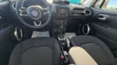 Driver’s-seat view of a Jeep interior: steering wheel with logo, central touchscreen, climate controls, gear shifter, and black fabric seats