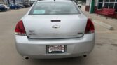 Rear view of a silver Chevrolet Malibu parked in a dealership lot, with a Wheel City license plate frame and a teal sale sign on the rear window.