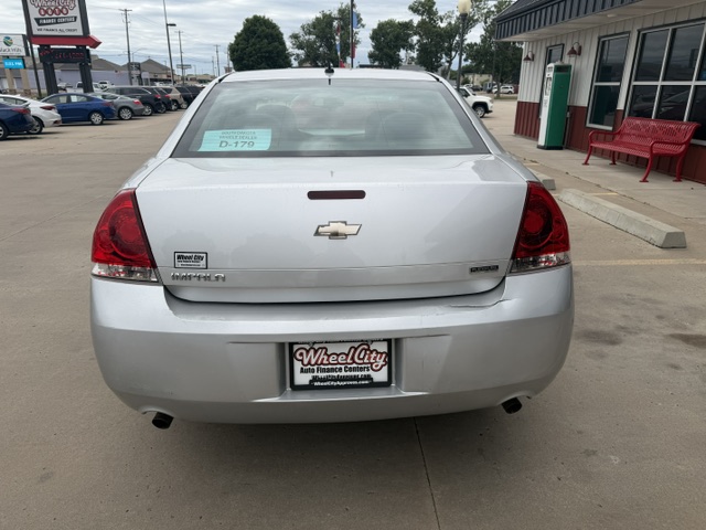 Rear view of a silver Chevrolet Malibu parked in a dealership lot, with a Wheel City license plate frame and a teal sale sign on the rear window.