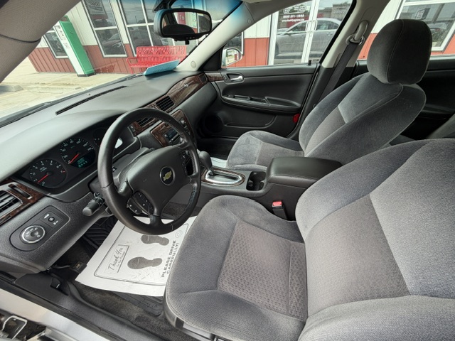 Front interior of a Chevrolet sedan showing steering wheel, driver and passenger seats, center console, and dashboard features.