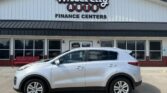 Silver crossover SUV parked in front of a Wheel City Auto Finance Centers storefront with large glass doors and red bench nearby.