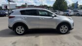 Side view of a silver 4-door SUV in a dealership lot, with neighboring cars and a blue sky above.