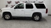 Side view of a white Chevrolet Tahoe LT parked indoors against a Wheel City banner backdrop in a showroom