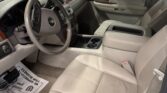 Beige leather interior of a Chevrolet SUV, showing the steering wheel, dashboard, center console, and front passenger seat with a dealer backdrop outside the window.