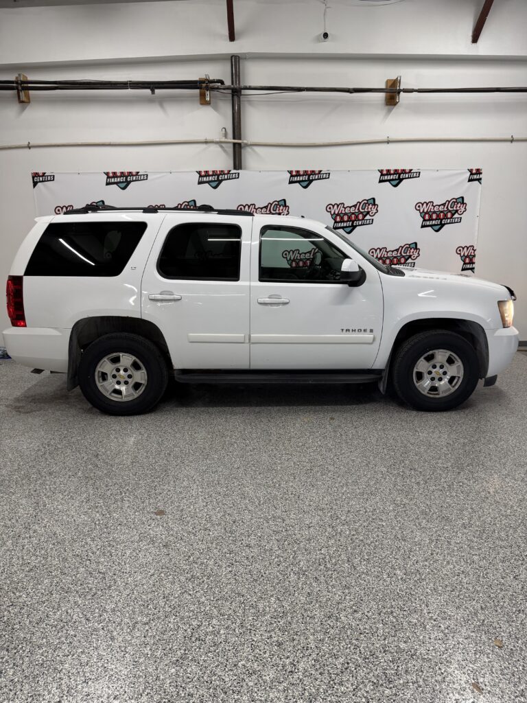 White Chevrolet Tahoe SUV parked indoors in front of a Wheel City Auto banner backdrop.