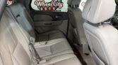Interior of a gray leather back seat area in a car, with headrests and seat belts visible ahead of a window showing a Wheel City Auto sign.