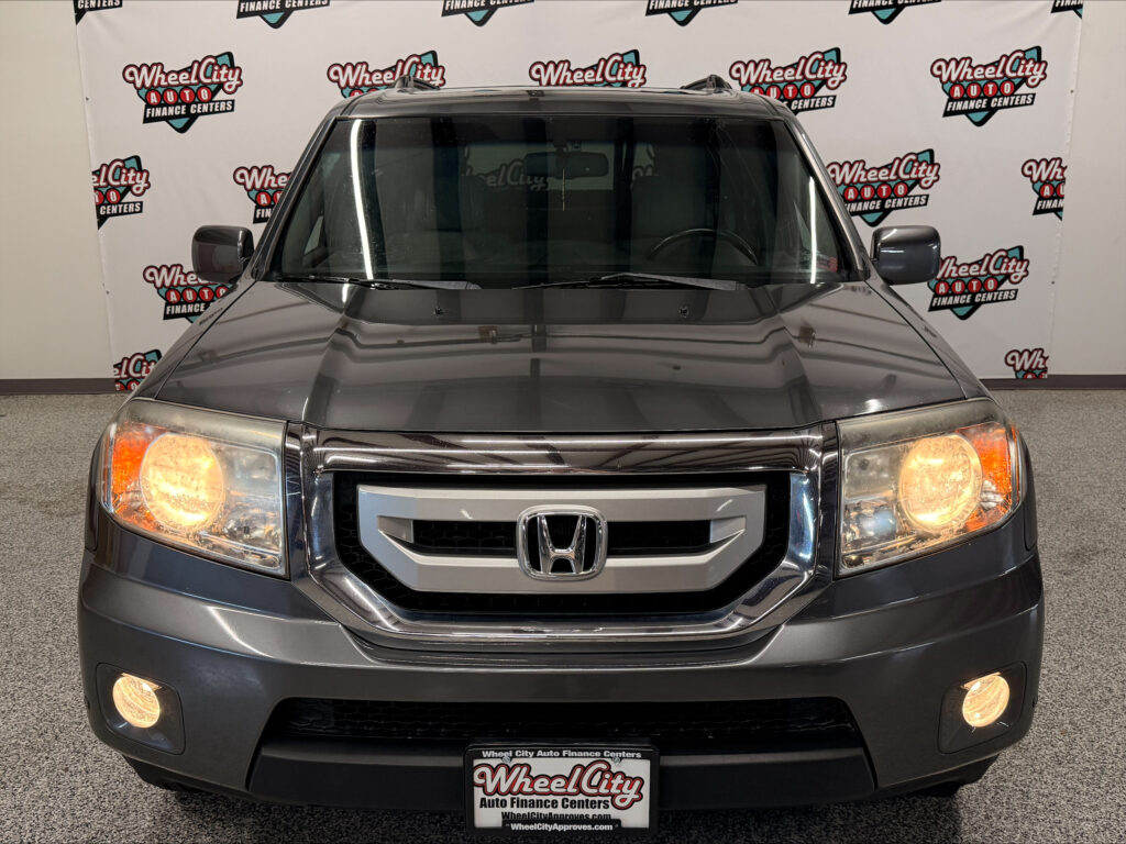 Front view of a gray Honda SUV at a car dealership, headlights on, with Wheel City Auto Finance Centers backdrop and front license plate area visible