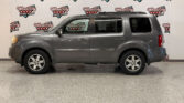 Side view of a gray full-size SUV indoors, in front of a Wheel City Auto Finance Centers backdrop.