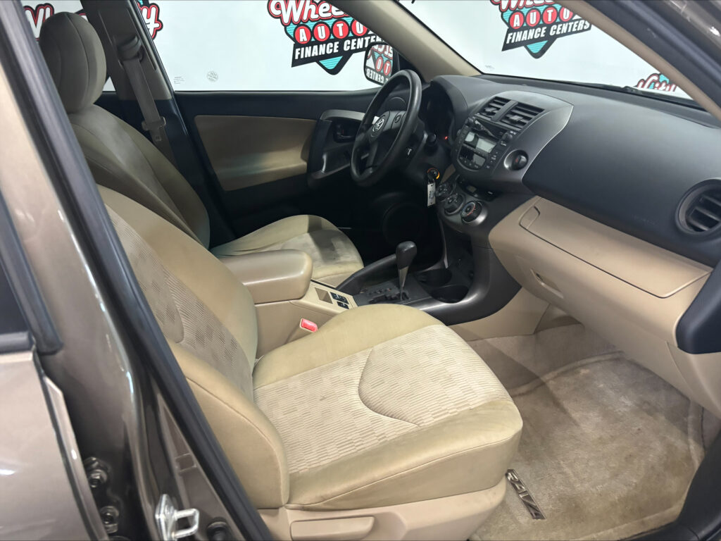 Interior of a beige sedan: driver and front passenger seats, steering wheel, center console, and dashboard.