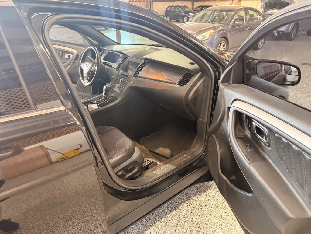 Interior of a dark SUV with the driver's door open, showing steering wheel, dashboard, center console, and front seats in a showroom.