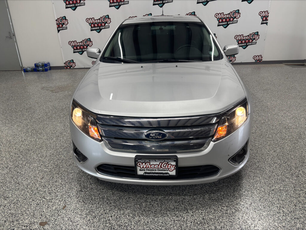 Front view of a silver Ford SUV in a showroom, with a Wheel City Auto Finance Centers banner in the background and license plate visible at the bottom left corner of the image.