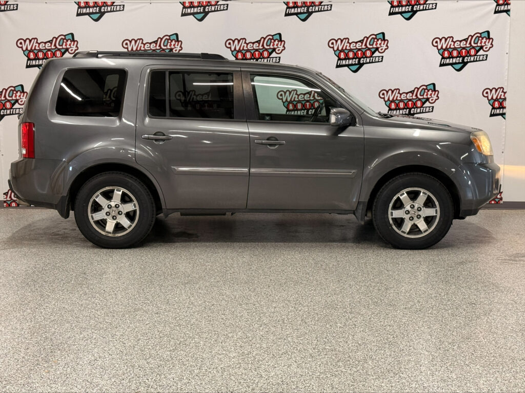 Side view of a gray Honda SUV with roof rails parked indoors in front of a Wheel City Auto Finance Centers backdrop.