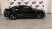 Black sedan parked indoors in front of a Wheel City Auto banner wall showroom backdrop, side profile view.