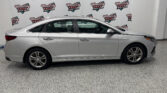 Side profile of a silver sedan parked indoors in front of a Wheel City Auto Finance Centers backdrop banner.