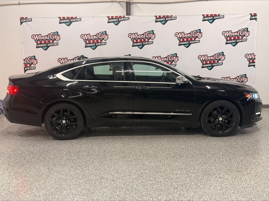 Side view of a black Chevrolet Impala in a showroom, with a Wheel City Auto Finance Centers backdrop behind the car.