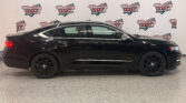 Side view of a black Chevrolet Impala in a showroom, with a Wheel City Auto Finance Centers backdrop behind the car.