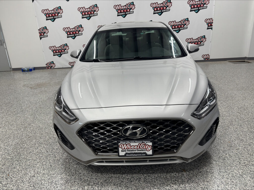 Front view of a silver Hyundai SUV in a showroom with a Wheel City Auto Finance Centers backdrop behind it.