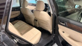Back seat area of a beige leather SUV interior with front seats visible and open rear door.