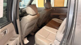 Open rear passenger door view of a tan leather SUV interior, showing second-row seats and center console