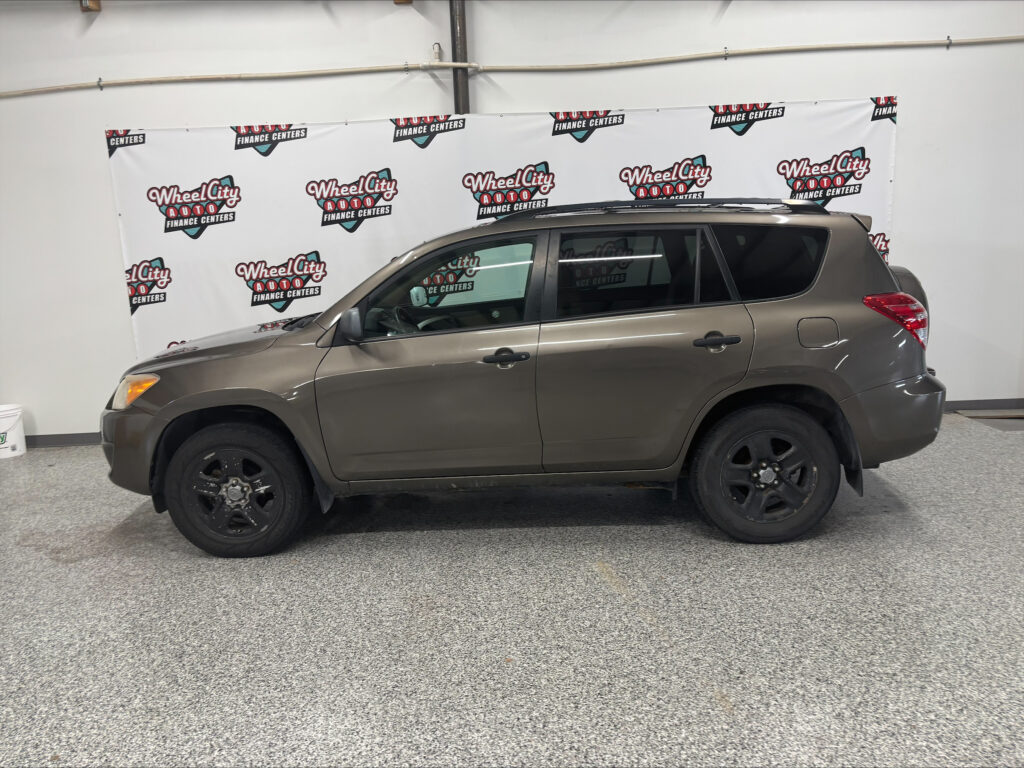 Taupe SUV parked indoors in a showroom with a repeated Wheel City Auto Finance Centers banner in the background.