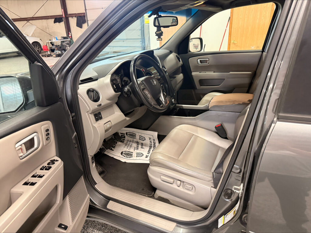 Interior of a gray SUV with the driver’s door open, showing steering wheel, dash, center console, and beige front seats.