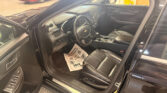 Interior of a black SUV with the driver's door open, showing leather front seats, steering wheel, and center console; paper mat on the floor; showroom with a red car in the background.