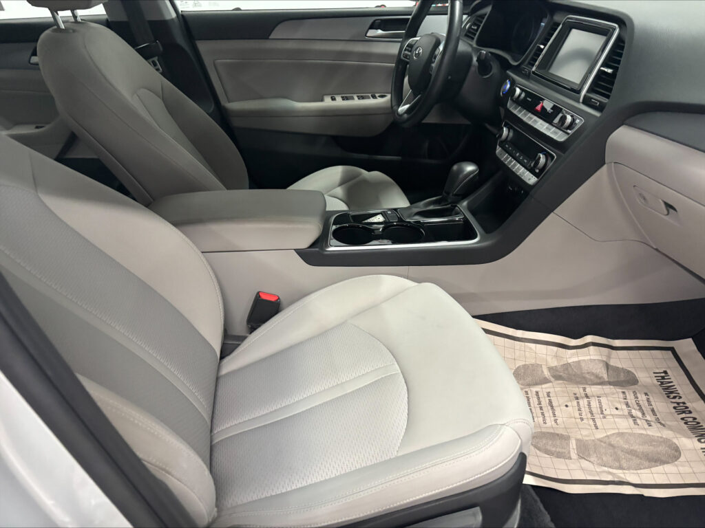 Interior of a car showing two front seats, light gray upholstery, and a center console with gear shifter and cupholders.