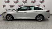 Side view of a silver sedan parked indoors in front of a Wheel City Auto Finance Centers backdrop banner(s)