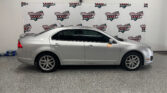 Side profile of a silver sedan parked indoors with a Wheel City Auto Finance Centers banner backdrop behind it.