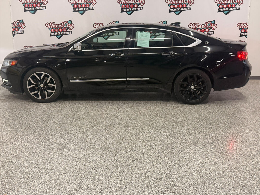 Black Chevrolet Impala sedan in a showroom, side profile with chrome trim and tinted windows, Wheel City Auto Finance Centers backdrop behind.
