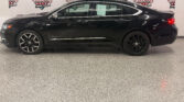 Black Chevrolet Impala sedan in a showroom, side profile with chrome trim and tinted windows, Wheel City Auto Finance Centers backdrop behind.