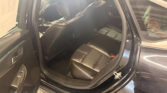 Rear passenger area of a black sedan with leather seats and orange stitching, door open for view of interior pieces and center console edge.