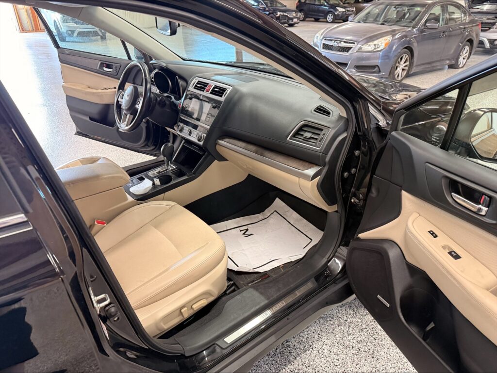 Open driver’s door shows beige leather interior and dashboard of a dark SUV inside a showroom.